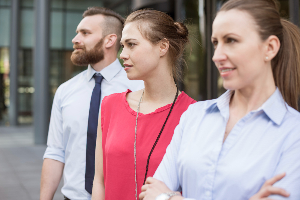 Three people stand confidently outdoors, looking in the same direction. They are dressed in business-casual attire.